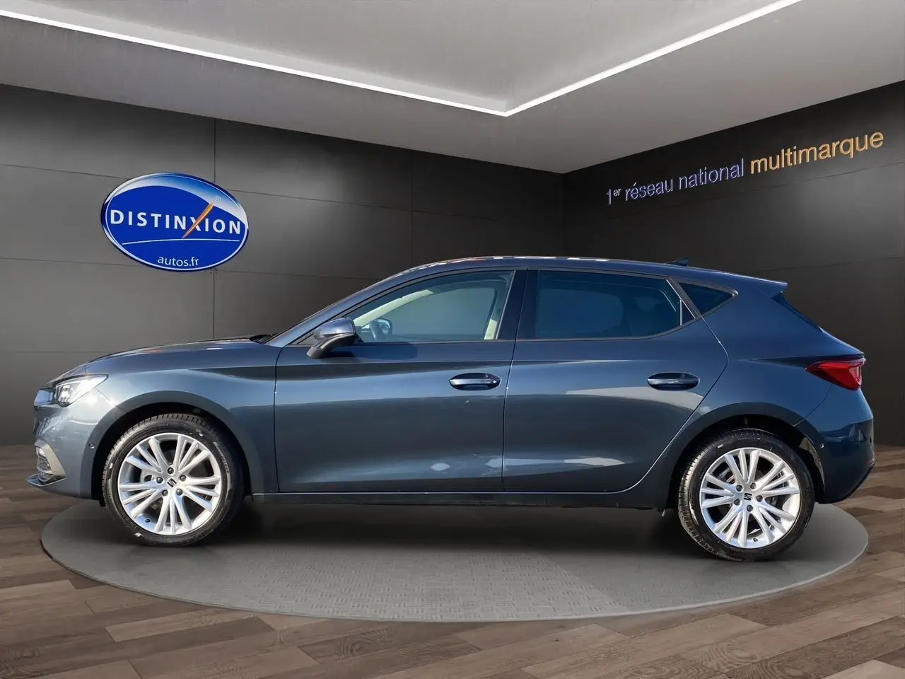 Vue latérale côté gauche d'une SEAT Leon IV gris magnetic avec jantes alu 17 pouces dans un showroom.