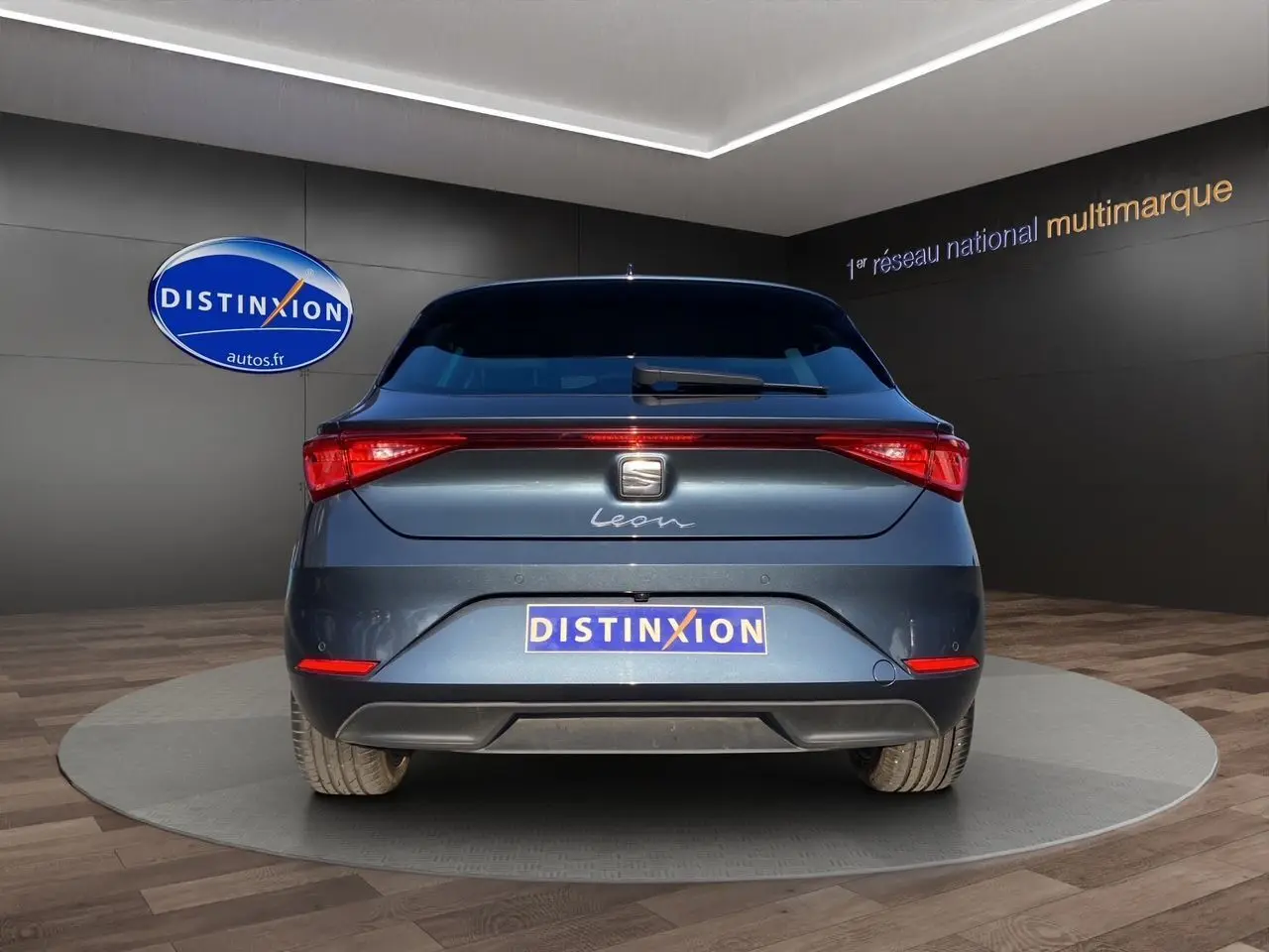 Vue arrière d'une SEAT Leon IV gris magnetic, avec feux LED et logo distinctif sur fond d'intérieur showroom.