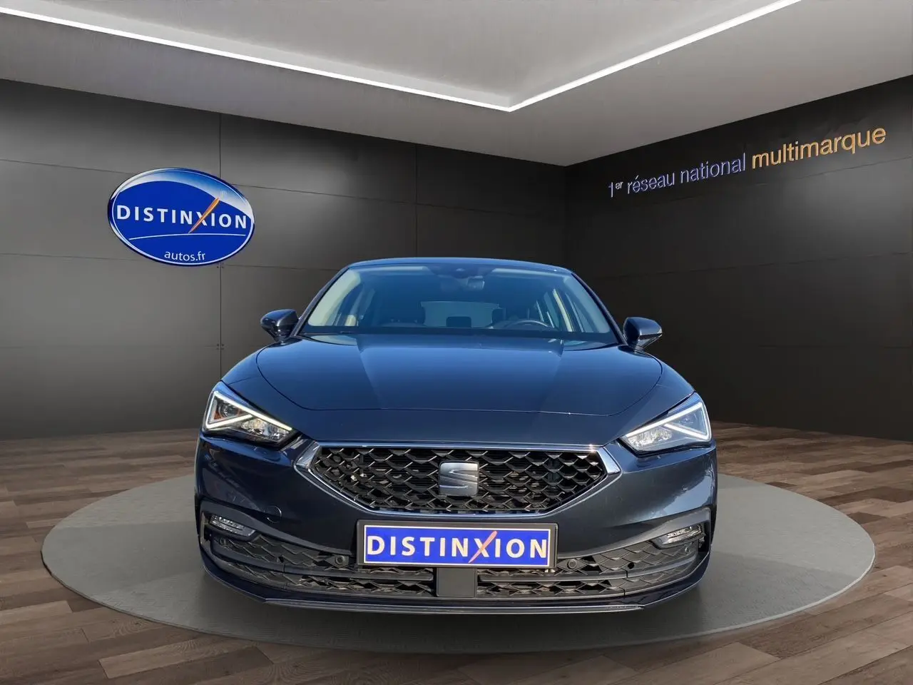 Vue frontale d'une SEAT Leon IV gris magnetic avec phares LED et calandre hexagonale en showroom.