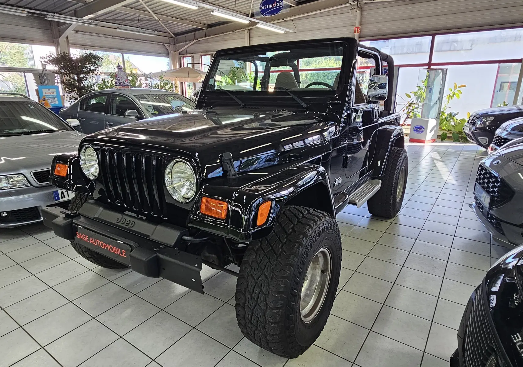 Jeep Wrangler noir de 2000 vu en 3/4 avant droit, avec toit ouvert et pneus tout-terrain marqués.