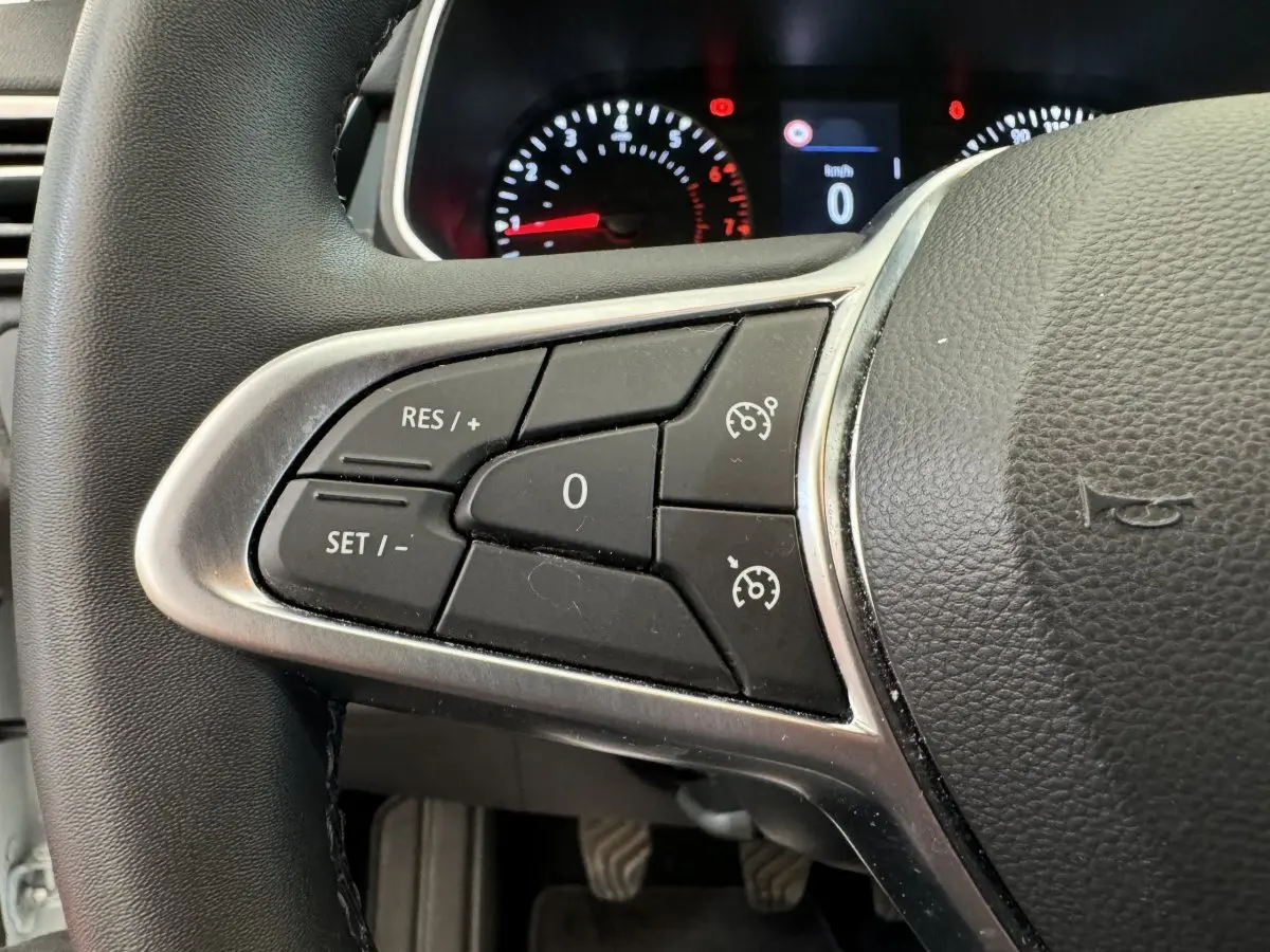 Gros plan sur les commandes du régulateur de vitesse à gauche du volant noir de la Renault Clio Business blanche de 2021.