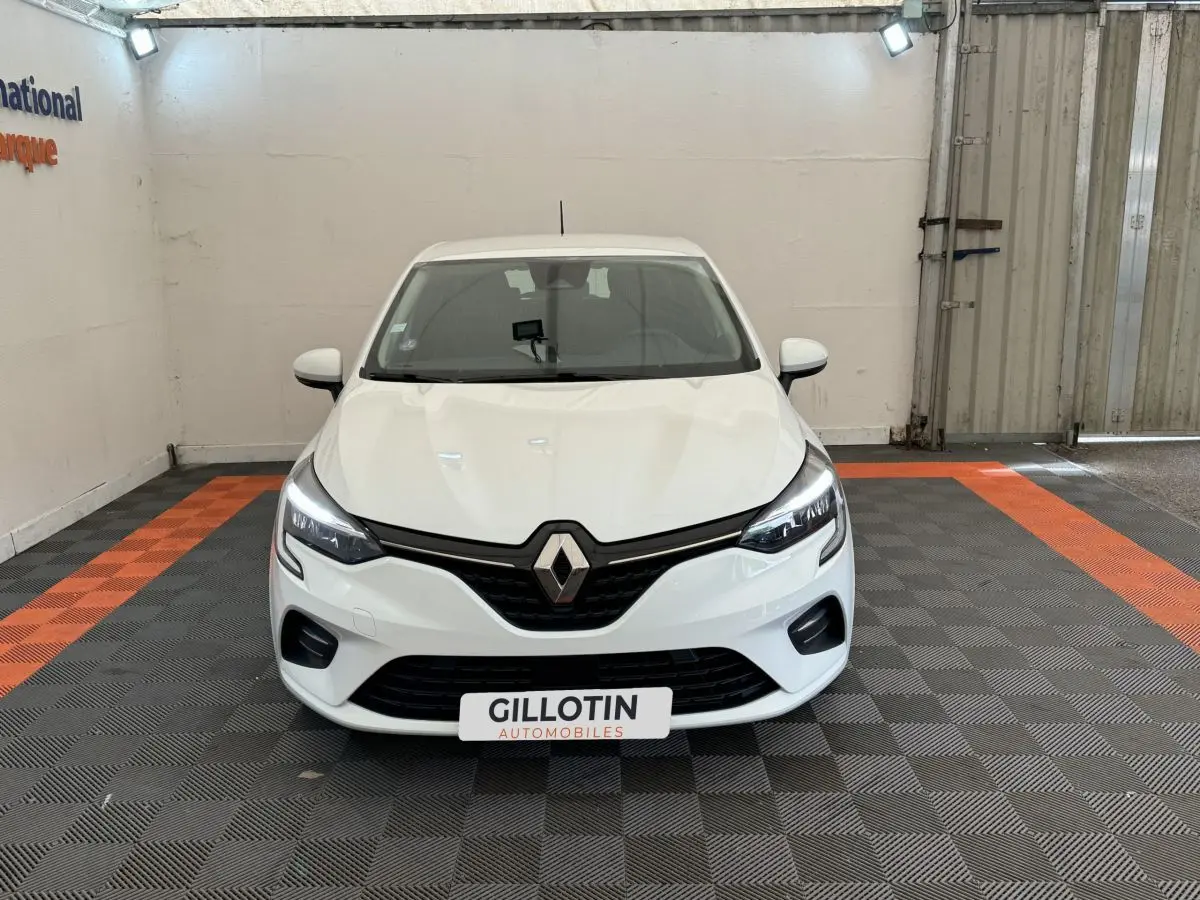 Vue avant d'une Renault Clio Business blanche avec phares LED allumés dans un garage éclairé.