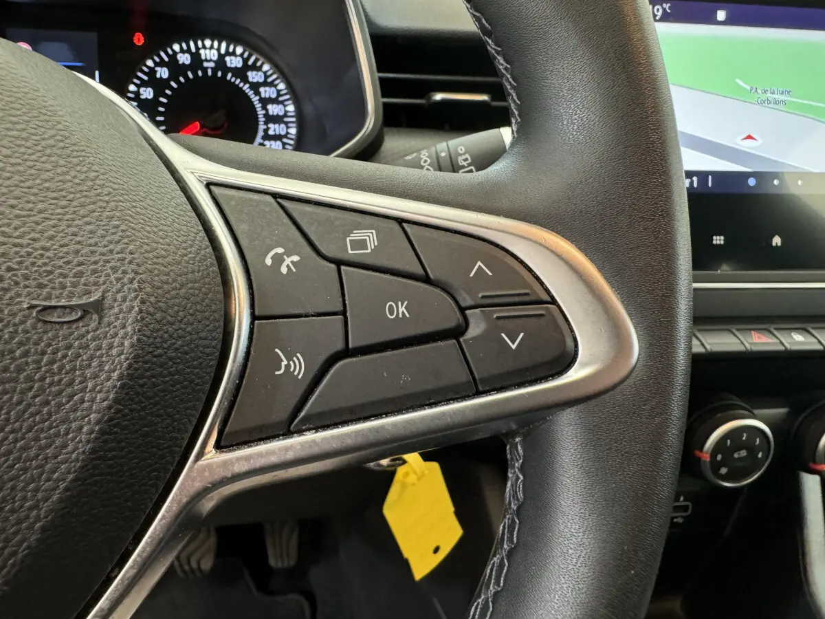 Gros plan sur les commandes du volant côté droit de la Renault Clio Business blanche, avec écran tactile et tableau de bord visible.