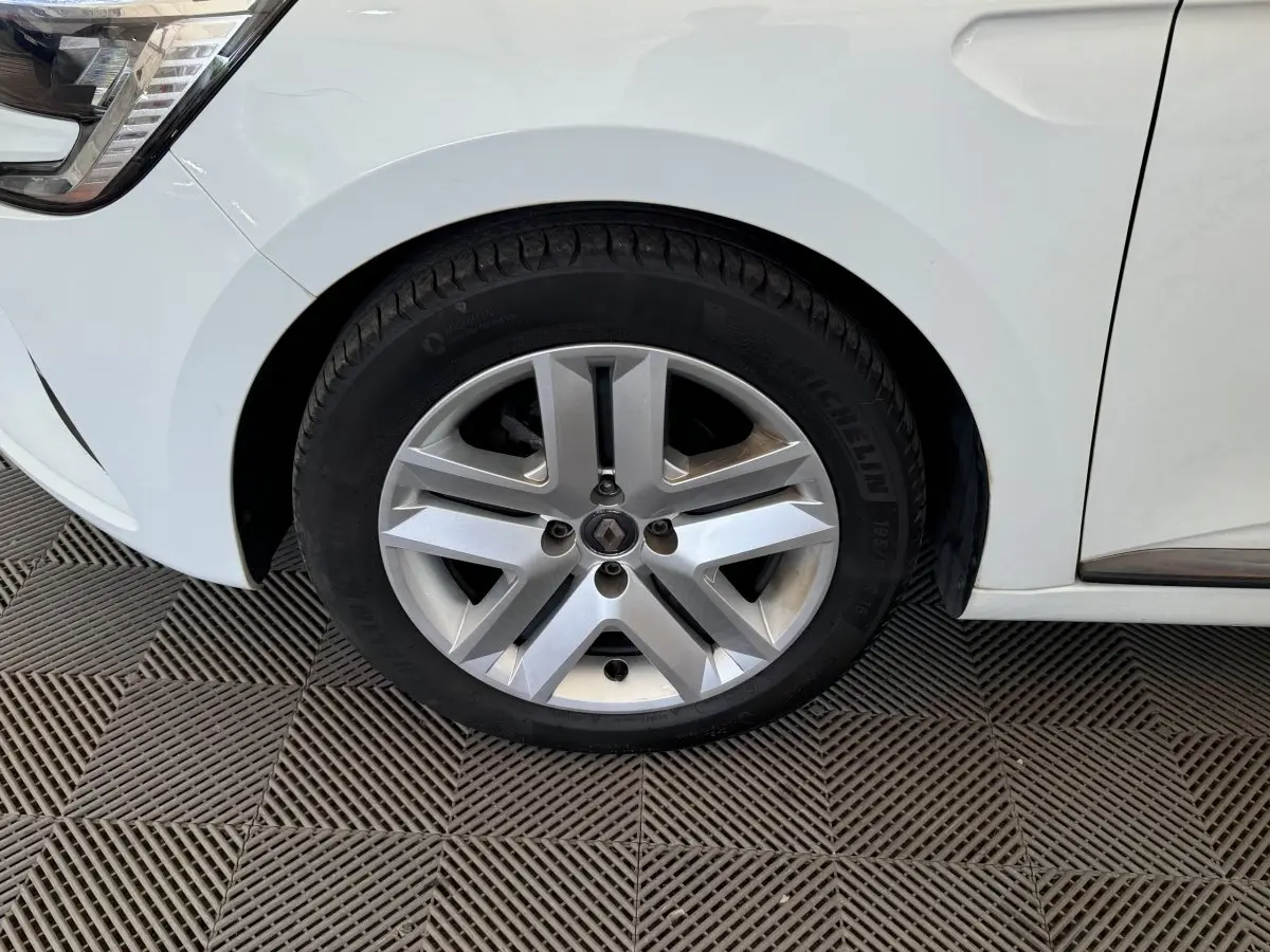 Gros plan sur la roue avant gauche blanche d'une Renault Clio Business 2021 avec jante alliage et logo Renault central.