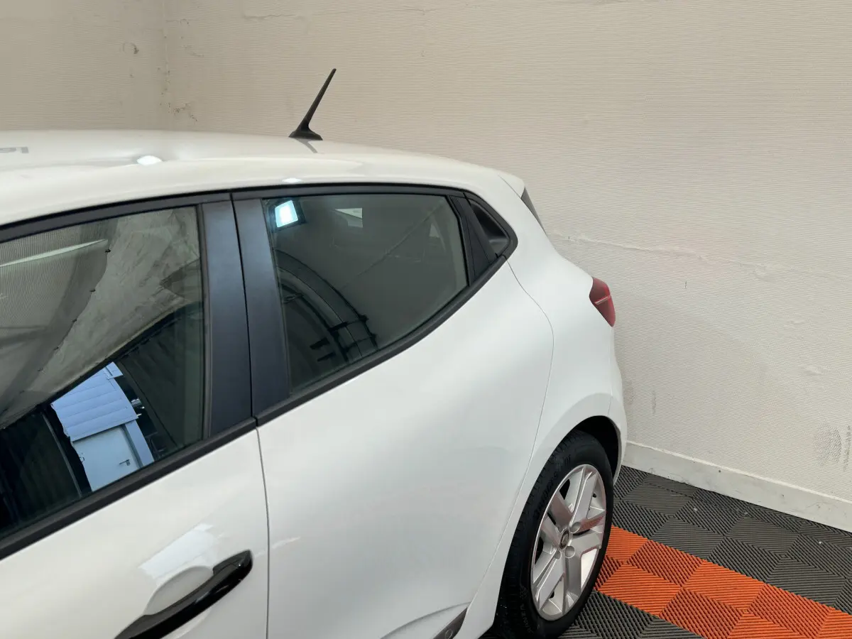 Vue côté gauche arrière d'une Renault Clio Business blanche avec poignées de porte noires et jantes alliage.