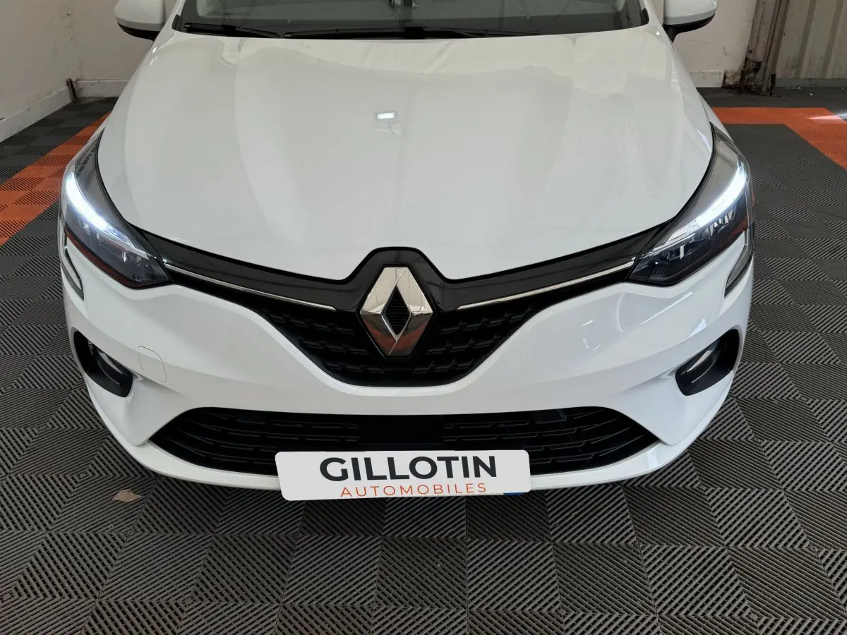 Vue frontale rapprochée d'une Renault Clio Business blanche avec phares LED allumés et calandre noire distinctive.