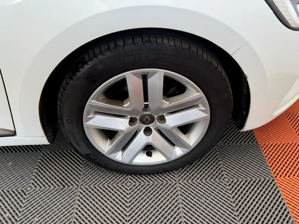 Gros plan sur la roue avant gauche blanche d'une Renault Clio Business 2021 avec jante alliage et logo Renault central.