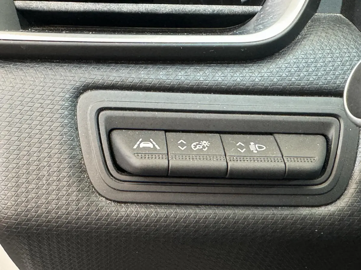 Gros plan sur les boutons de réglage d'assistance et d'éclairage du tableau de bord noir de la Renault Clio Business blanche.