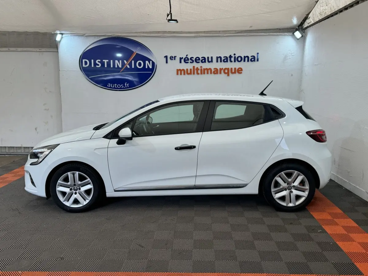Profil droit d'une Renault Clio Business blanche 2021, stationnée en intérieur sur sol gris et orange, avec logo Distinxion en arrière-plan.