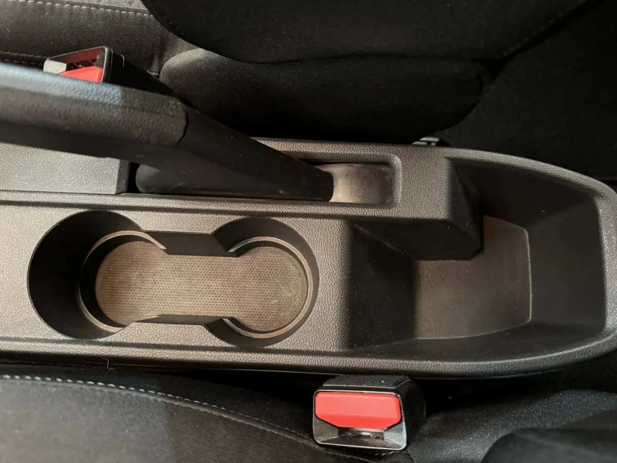 Gros plan sur la console centrale noire de la Renault Clio Business blanche, avec frein à main et porte-gobelets visibles.