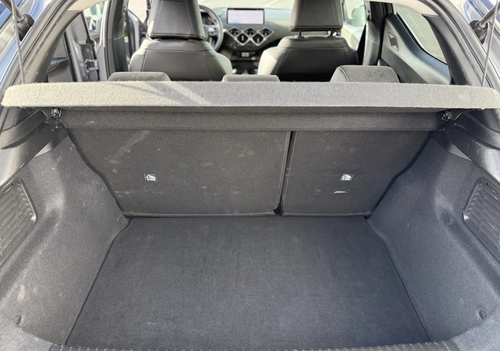Coffre ouvert vu de l'arrière d'une DS3 hybride 2025 gris Artense toit noir, montrant l'intérieur et les sièges arrière.