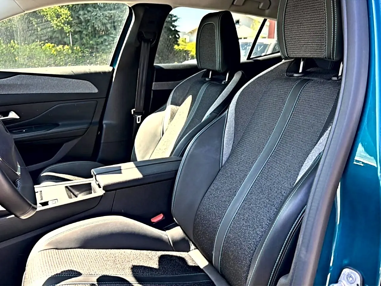 Vue intérieure côté conducteur du Peugeot 408 Hybrid 145 allure e-dcs6 bleu, sièges tissu et cuir avec accoudoir central.