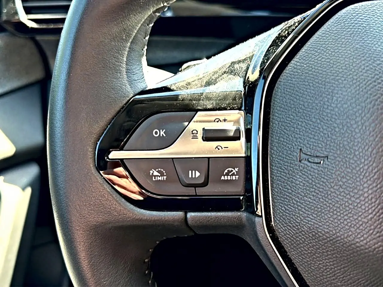 Gros plan sur les commandes gauche du volant cuir noir du Peugeot 408 Hybrid 145 allure 2025, boutons de régulateur et limiteur.