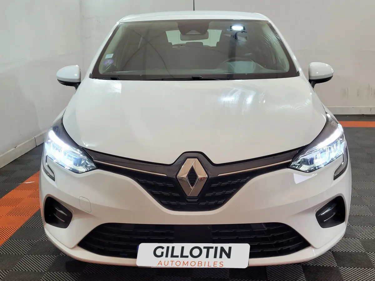 Vue frontale d'une Renault Clio Business blanche avec phares LED allumés et calandre noire distinctive.