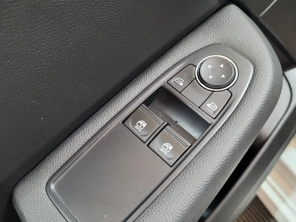 Gros plan sur les commandes de lève-vitres et réglage des rétroviseurs côté conducteur d'une Renault Clio Business blanche 2021.