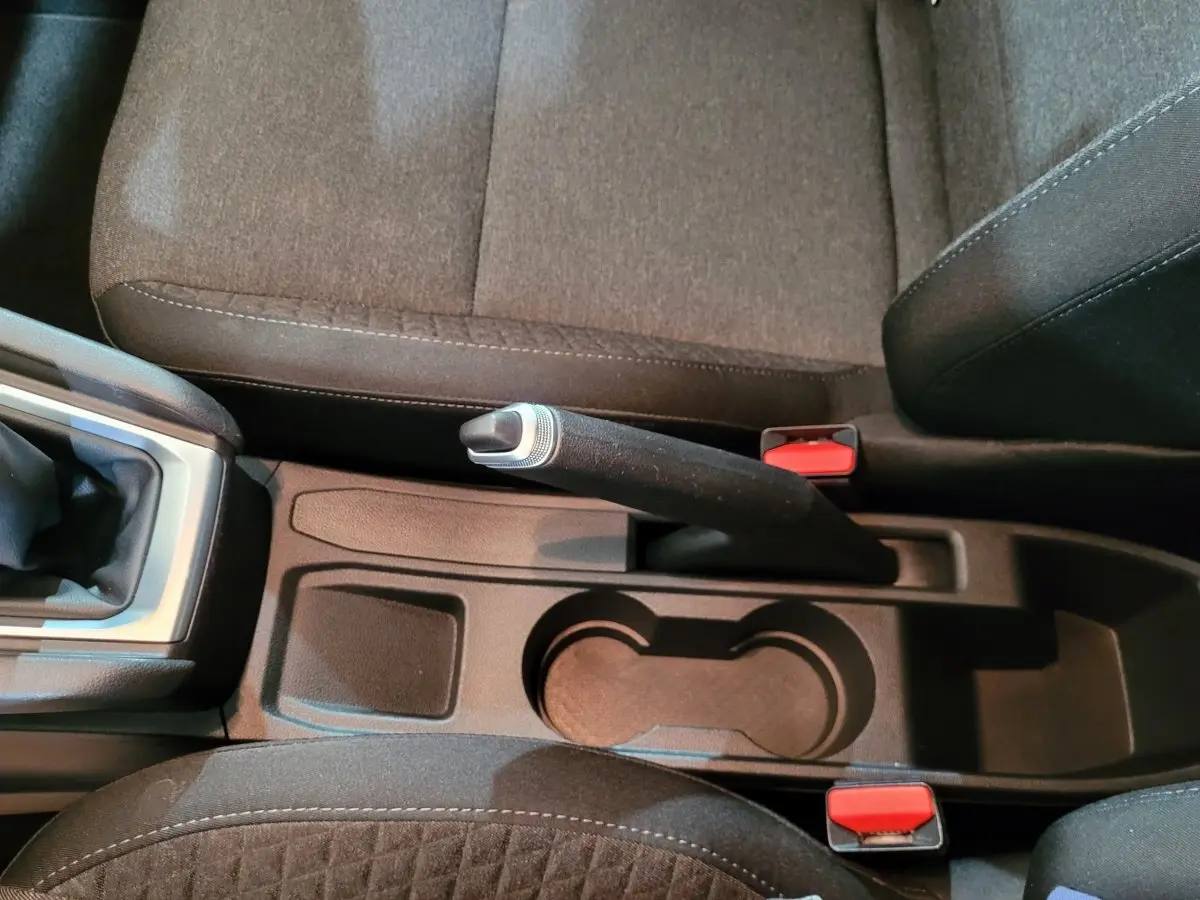 Vue rapprochée de la console centrale noire de la Renault Clio Business blanche, avec frein à main manuel et porte-gobelets.