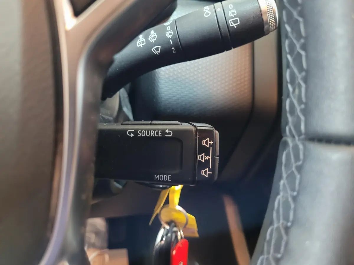 Gros plan sur la commande multimédia au volant d'une Renault Clio Business blanche, avec clé insérée et volant cuir visible.