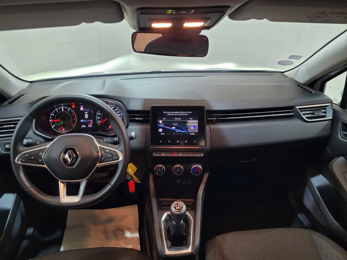 Vue intérieure avant du tableau de bord et volant cuir synthétique d'une Renault Clio Business blanche de 2021 avec écran tactile central.