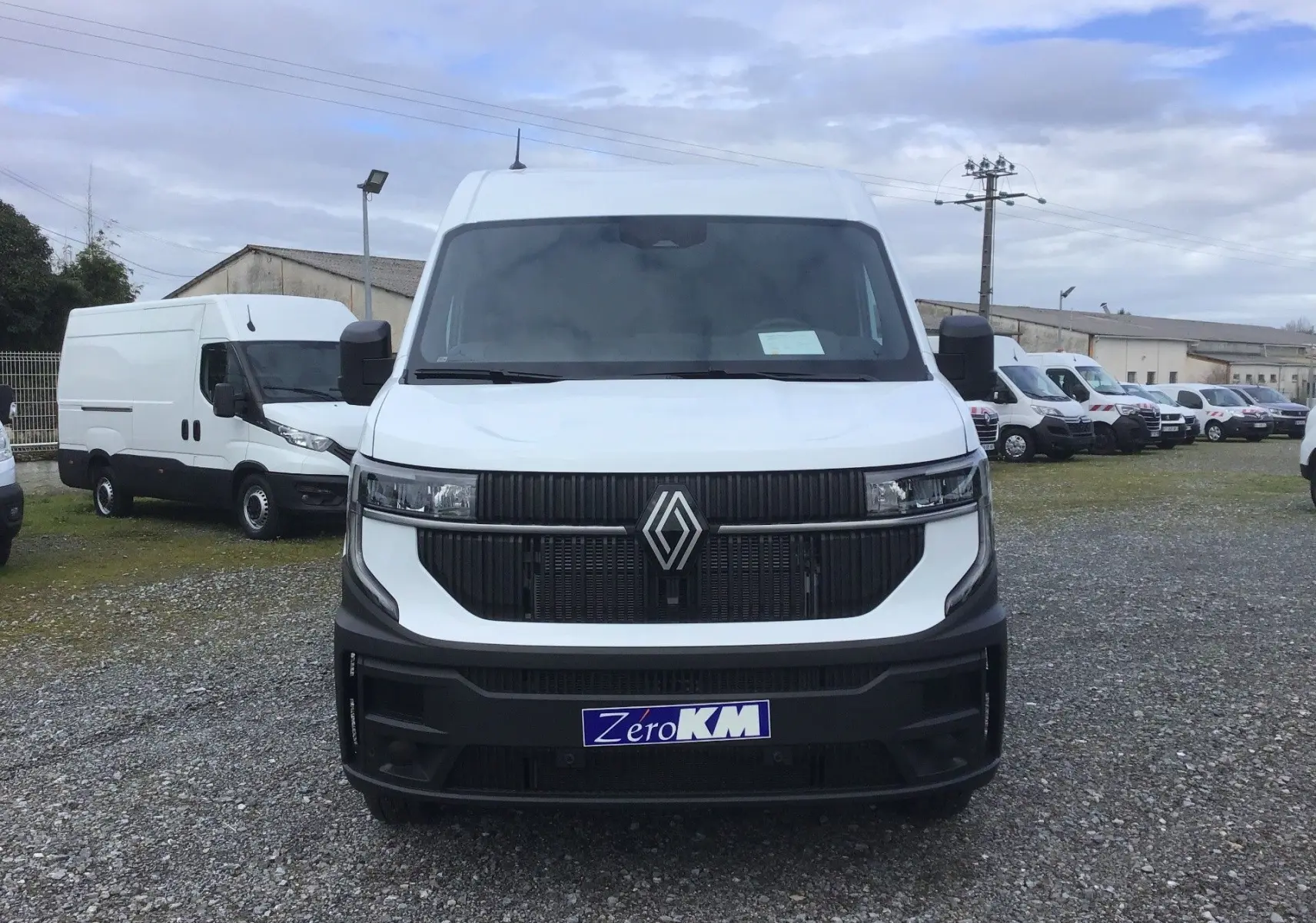 Vue frontale d’un Renault Master blanc 2026 avec calandre noire et logo Renault proéminent, stationné sur un terrain gravillonné.