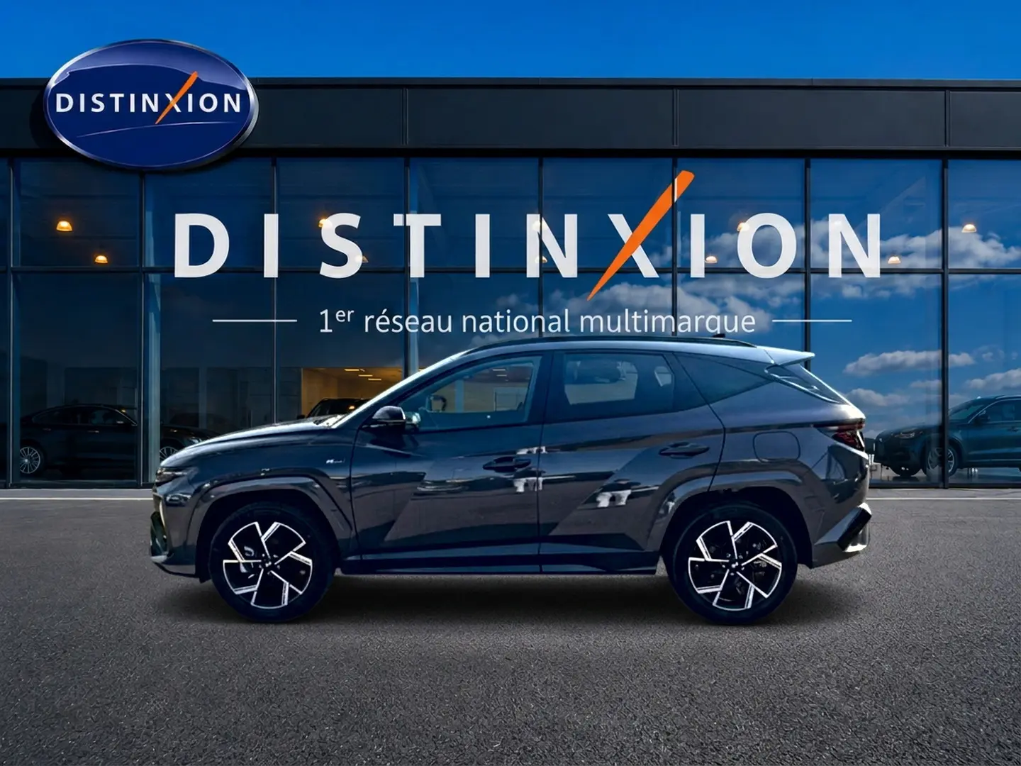 Vue de profil droit du Hyundai Tucson gris écotronique avec jantes alliage 19 et détails N Line devant une vitrine Distinxion.