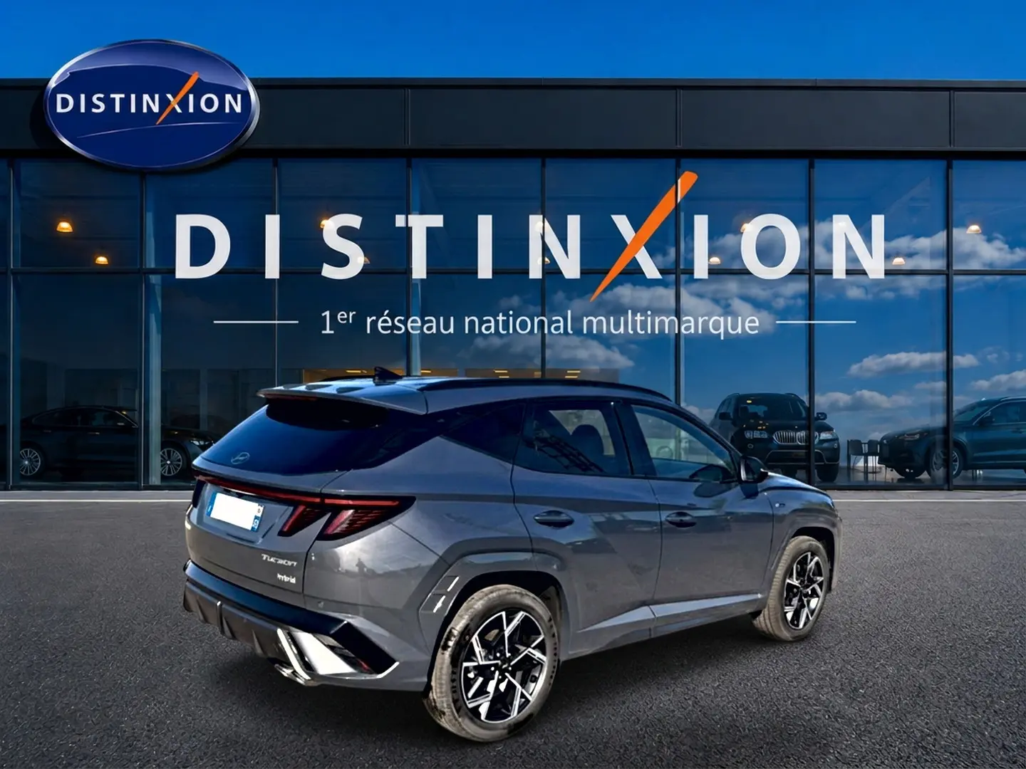Vue 3/4 arrière droite du Hyundai Tucson 2026 gris ecotronique avec jantes alliage et toit noir devant une vitrine Distinxion.