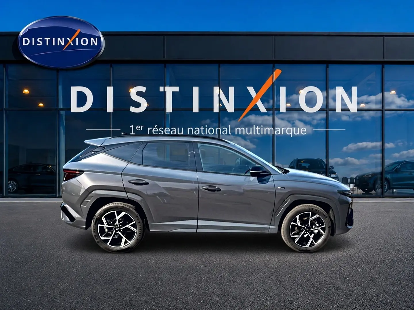 Hyundai Tucson 2026 gris écotronique en profil droit, avec jantes alliage 19 pouces et barres de toit visibles.