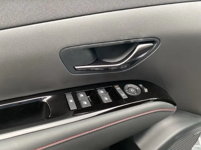 Détail de la porte côté conducteur du Hyundai Tucson gris foncé, avec commandes des vitres et poignée intérieure noire.