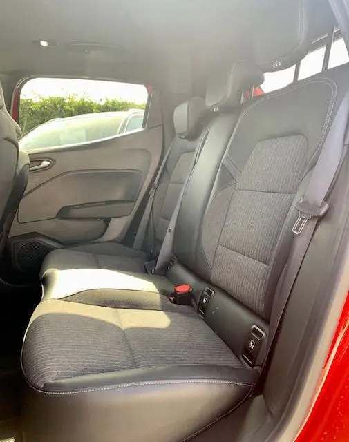 Vue latérale intérieure des sièges arrière en tissu et cuir d'une Renault Clio V rouge 2021, avec ceinture de sécurité visible.
