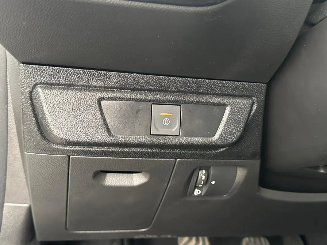 Détail intérieur du tableau de bord côté conducteur de la Dacia Sandero blanche 2024, avec bouton de fermeture centralisée éclairé.
