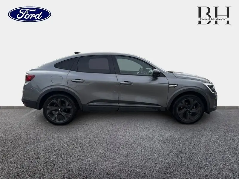 Profil côté gauche d'un Renault Arkana gris métallisé 2023 avec jantes noires et lignes dynamiques distinctives.