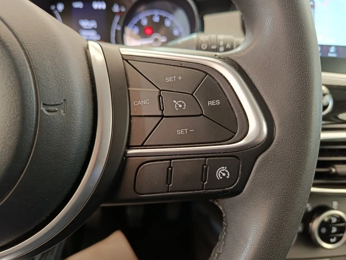 Gros plan sur les commandes du régulateur de vitesse au volant cuir noir de la FIAT 500X blanche, tableau de bord en arrière-plan flou.