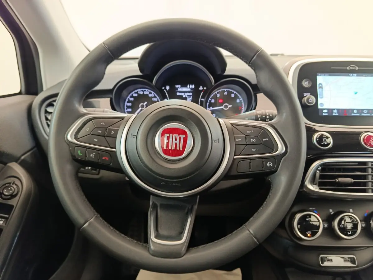 Vue intérieure centrée sur le volant noir cuir du Fiat 500X avec tableau de bord et écran tactile navigation visible à droite.