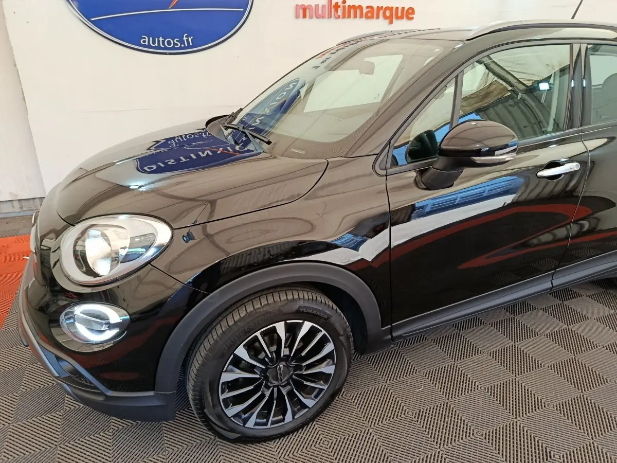 Vue 3/4 avant droit d'une FIAT 500X noire avec jantes noires et détails chromés sur les rétroviseurs et poignées.