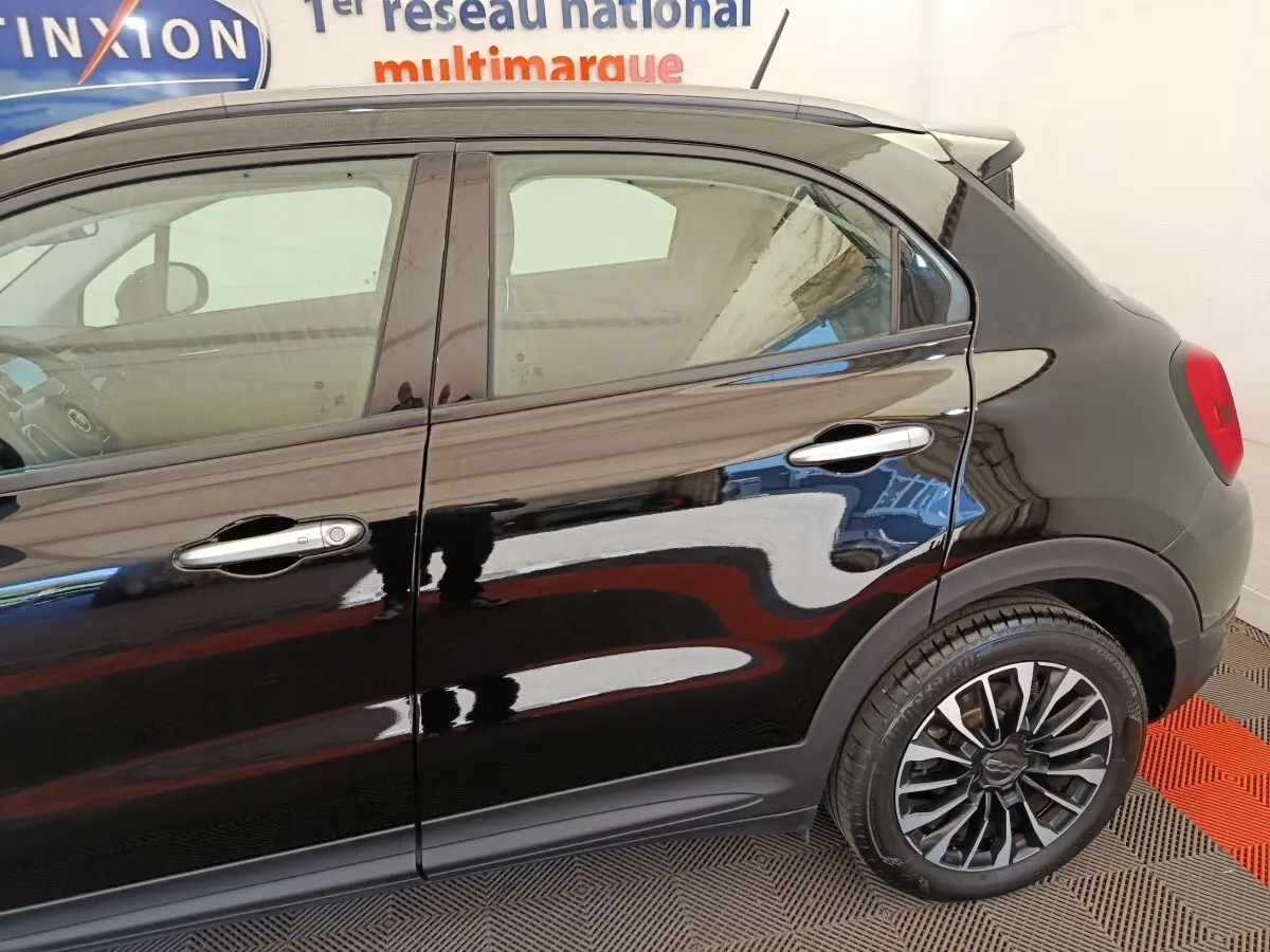 Vue latérale droite d'une FIAT 500X noire avec jantes alliage et poignées de porte chromées.