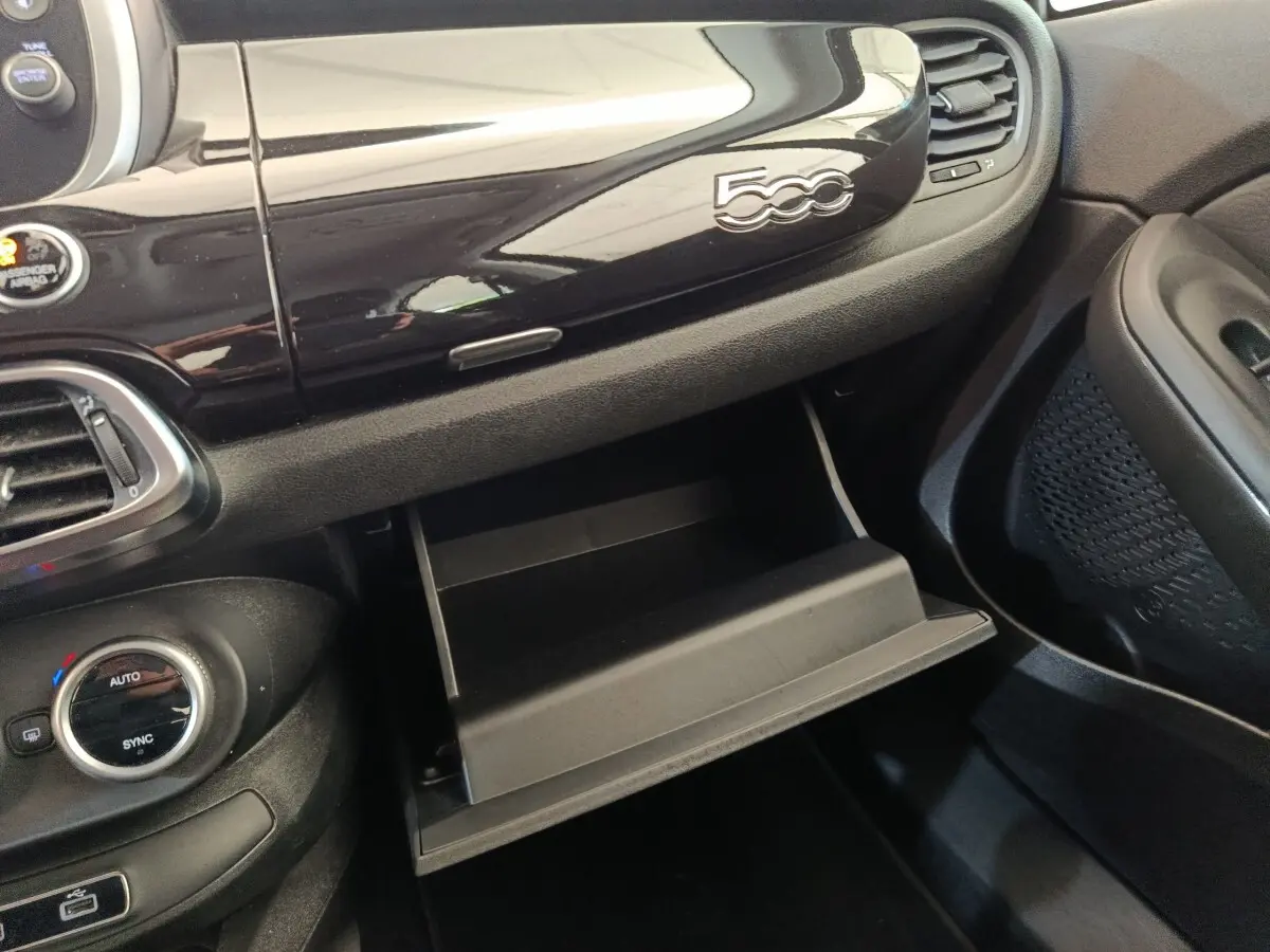 Gros plan sur la boîte à gants ouverte et le tableau de bord noir brillant avec logo 500 dans une Fiat 500X blanche.
