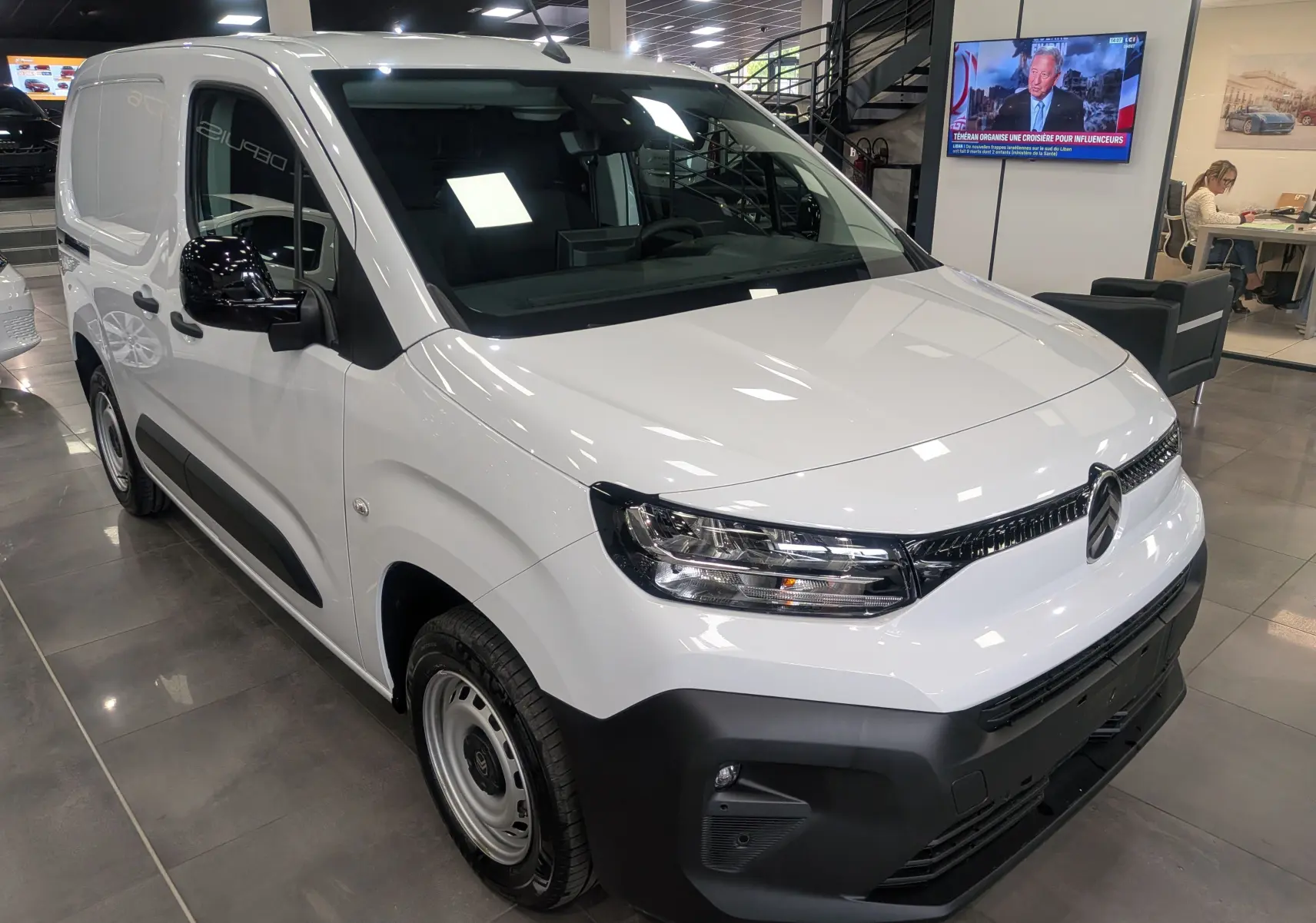 Vue 3/4 avant gauche d'un Citroën Berlingo Van blanc 2025 avec pare-chocs noir mat et rétroviseurs noirs en concession.
