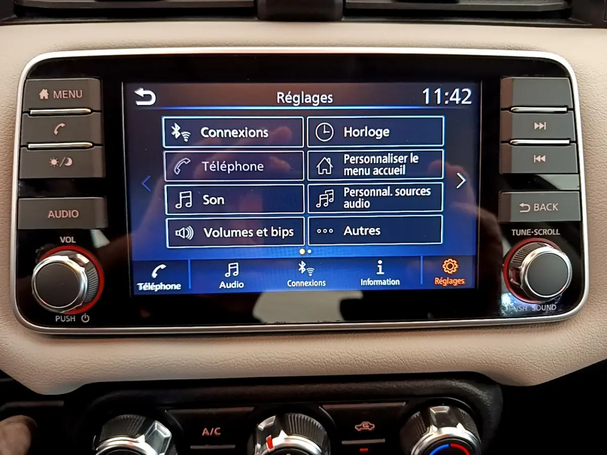 Écran tactile central affichant les réglages audio et connexions dans le tableau de bord beige d'une Nissan Micra blanche