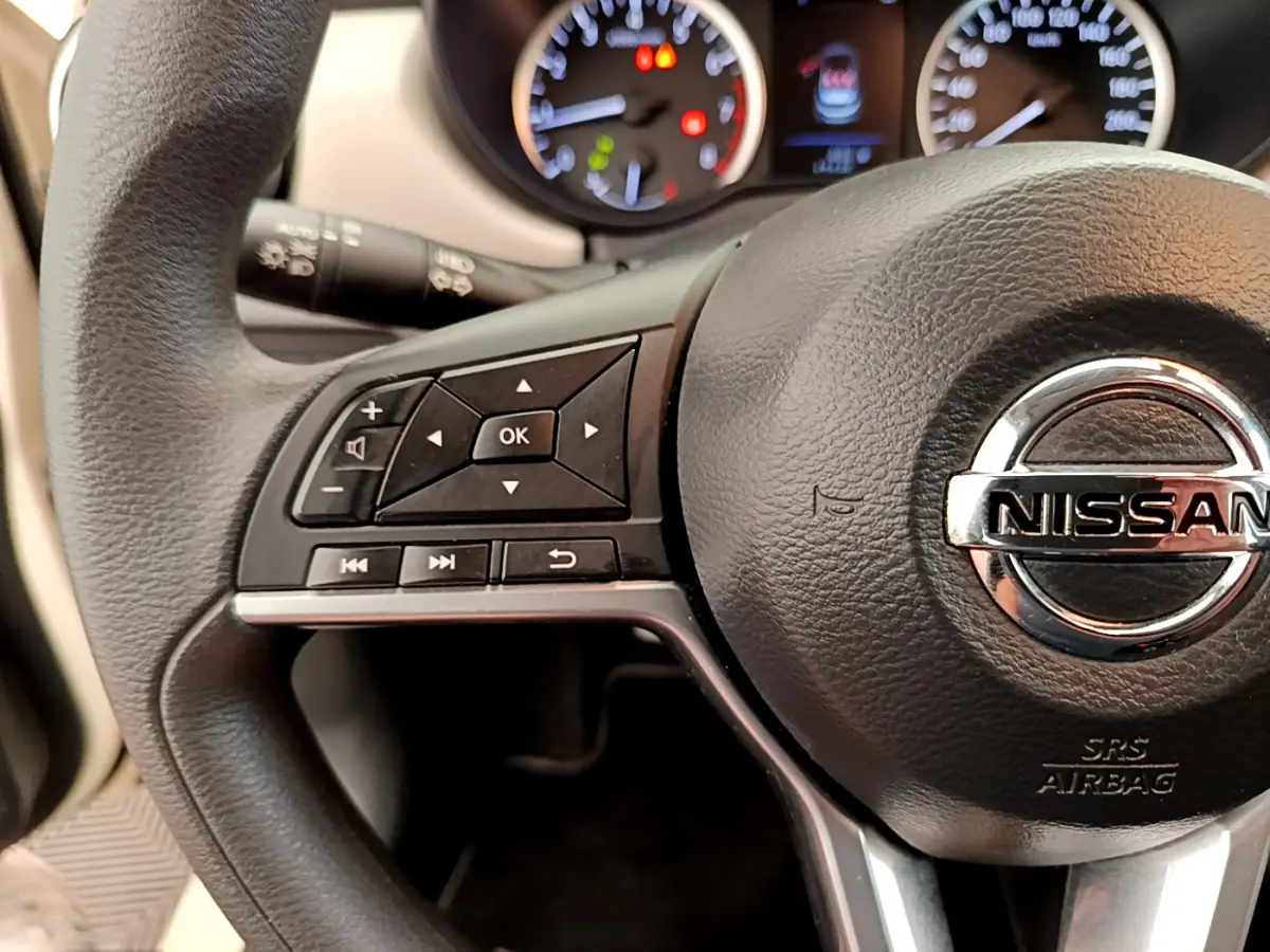 Gros plan sur le volant noir de la Nissan Micra 2022 avec commandes multifonctions et tableau de bord éclairé.