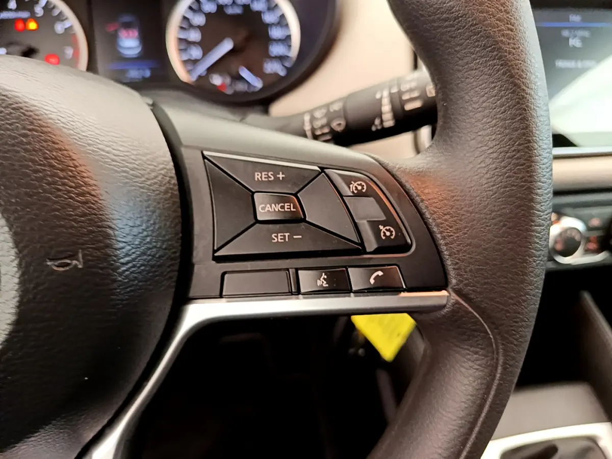 Gros plan sur les commandes du volant noir de la Nissan Micra IG-T 92 Acenta 2022, avec tableau de bord flou en arrière-plan.