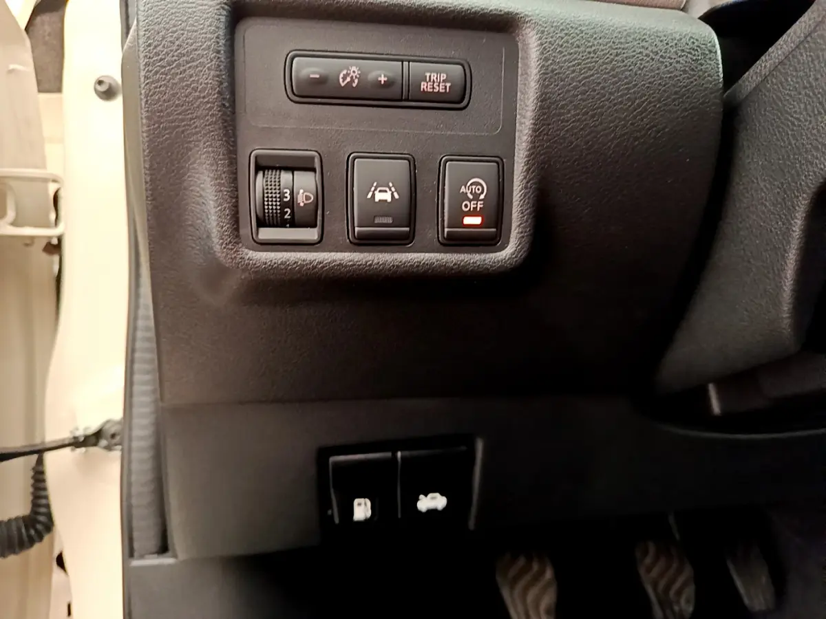 Vue rapprochée des commandes de réglage des phares et d'assistance sur le tableau de bord gauche d'une Nissan Micra blanche 2022.