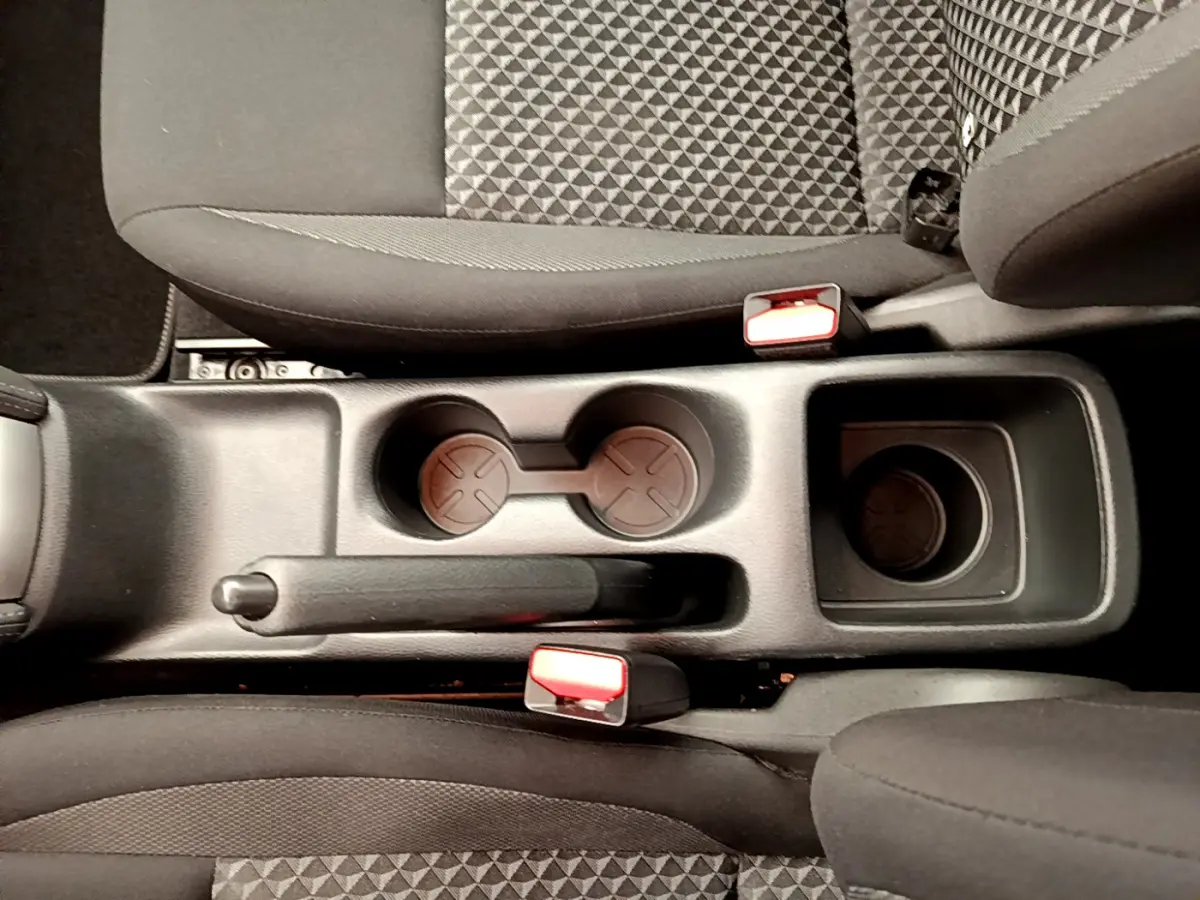 Vue plongeante sur la console centrale noire avec frein à main et porte-gobelets entre les sièges tissu gris de la Nissan Micra 2022.