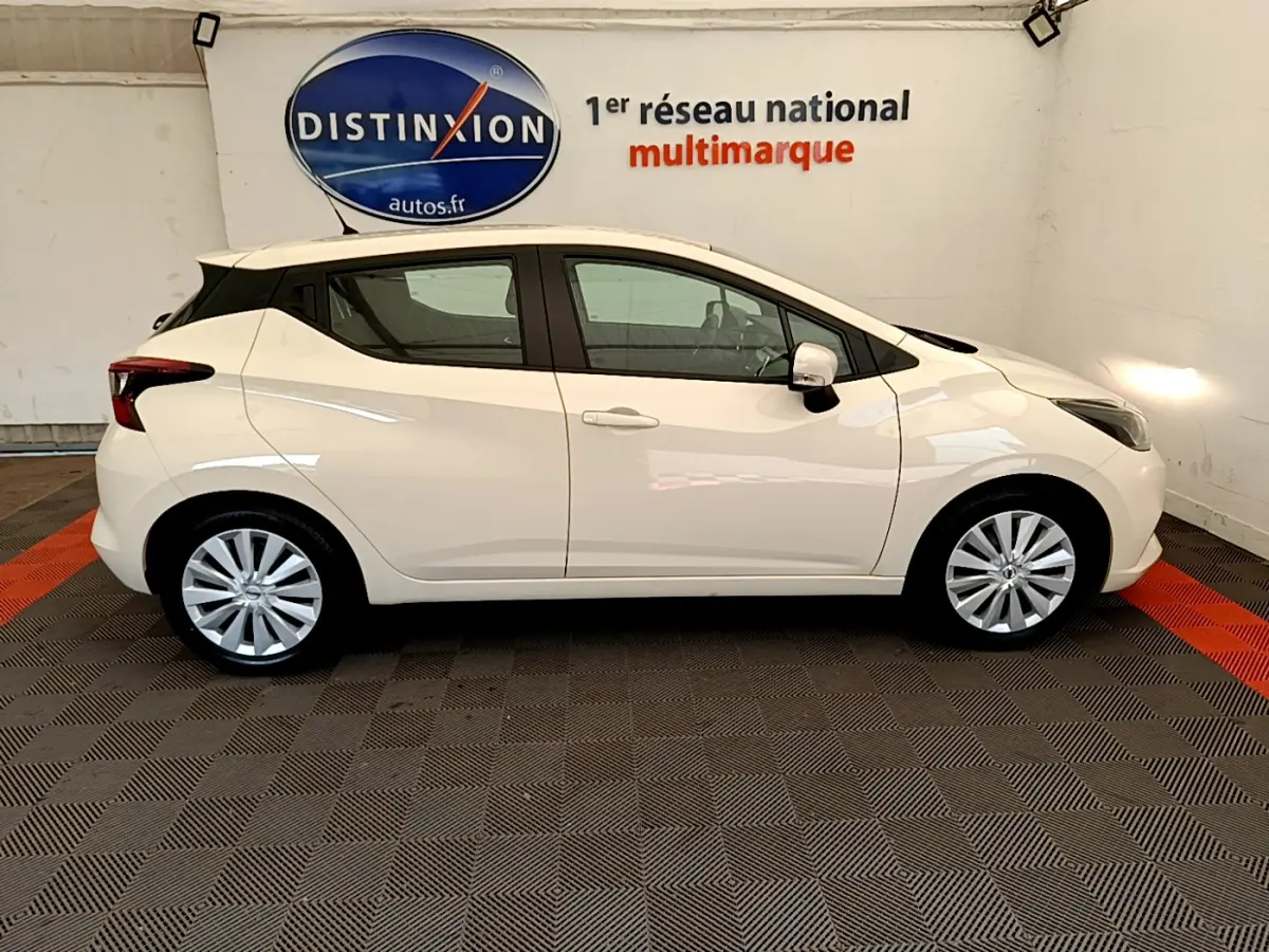 Profil côté droit d'une Nissan Micra blanche 2022 Acenta dans un showroom avec logo Distinxion en arrière-plan.