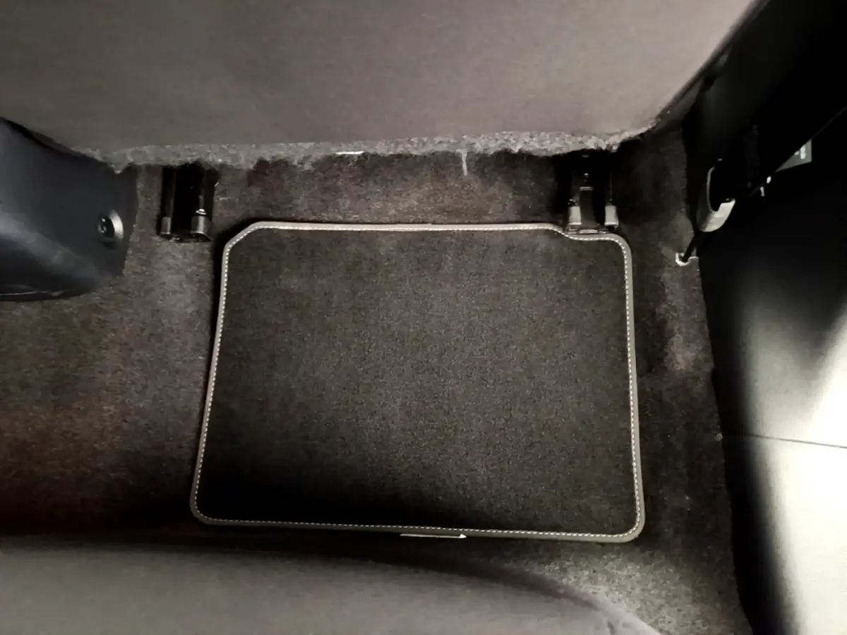 Tapis de sol noir avec surpiqûres blanches dans l'habitacle d'une Nissan Micra IG-T 92 Acenta blanche, vue intérieure au sol côté passager.