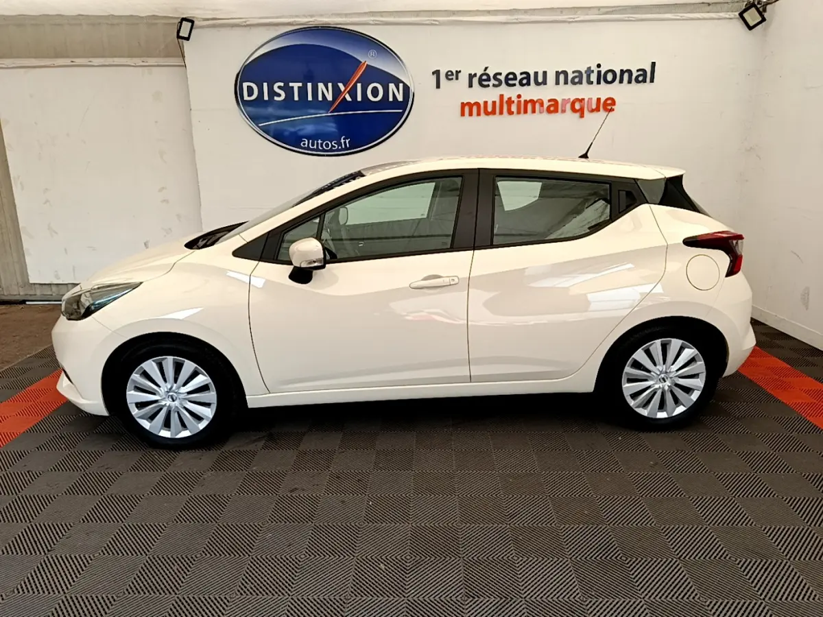 Profil latéral gauche d'une Nissan Micra blanche 2022 en intérieur, avec jantes alliage et toit noir contrastant.