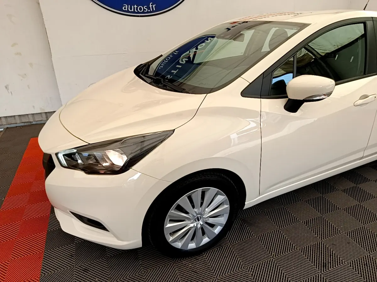 Vue 3/4 avant droit d'une Nissan Micra blanche 2022 avec phares allumés et jantes alliage visibles.