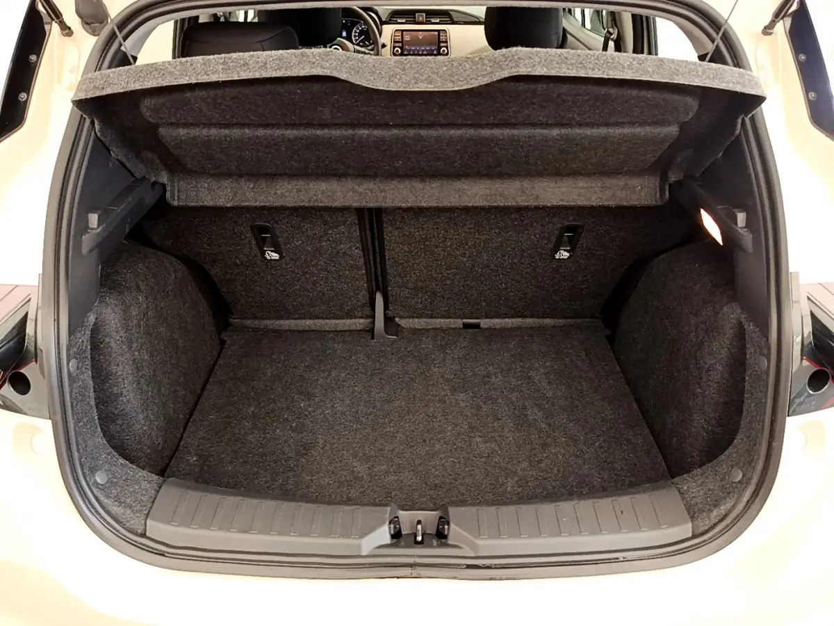 Coffre ouvert d'une Nissan Micra blanche, vue arrière montrant l'espace de chargement et la tablette de protection relevée.