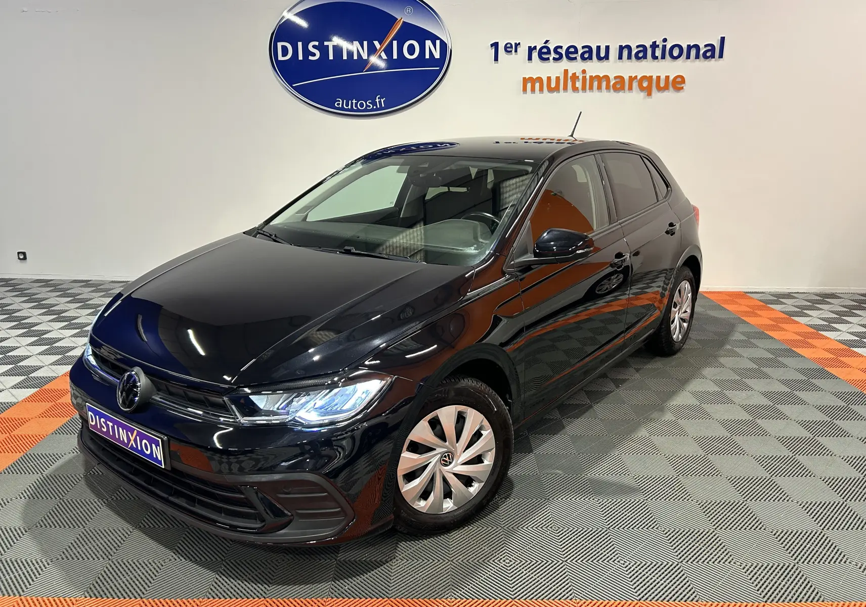 Volkswagen Polo noire vue en 3/4 avant droit, avec phares allumés dans un showroom lumineux.