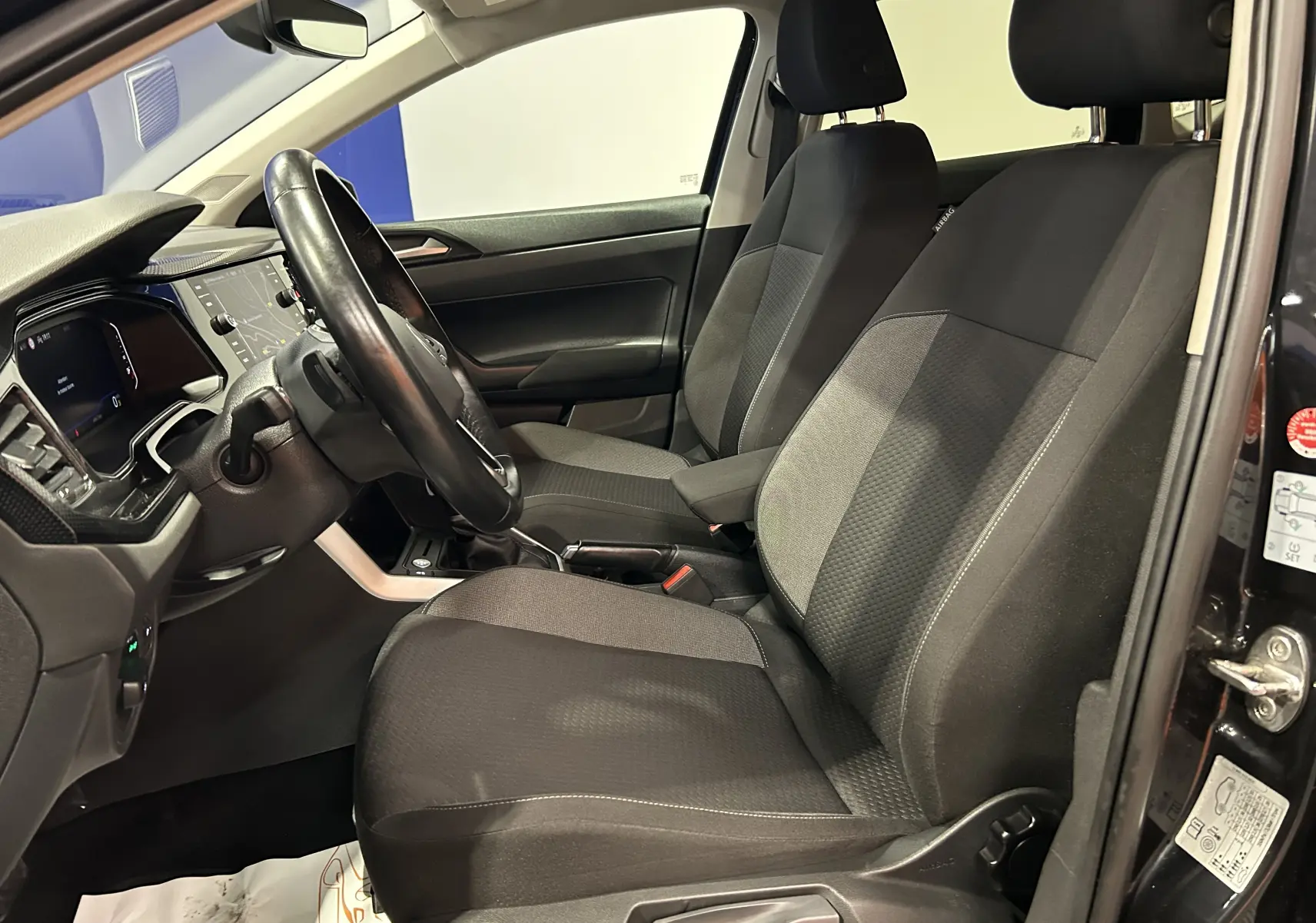 Vue intérieure côté conducteur de la Volkswagen Polo noire 2022, montrant sièges tissu et tableau de bord avec écran digital.