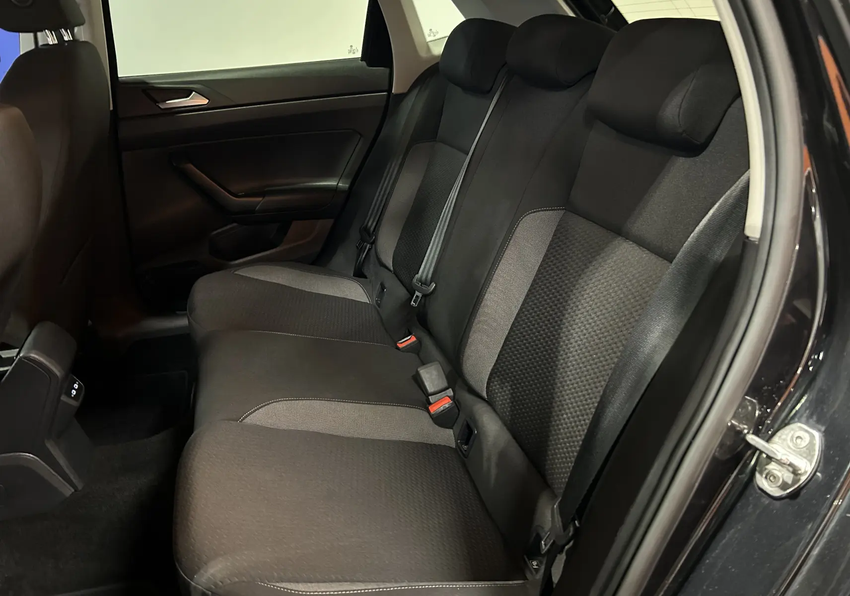 Vue intérieure côté arrière droit de la Volkswagen Polo noire 2022, montrant les sièges arrière en tissu avec ceintures de sécurité.