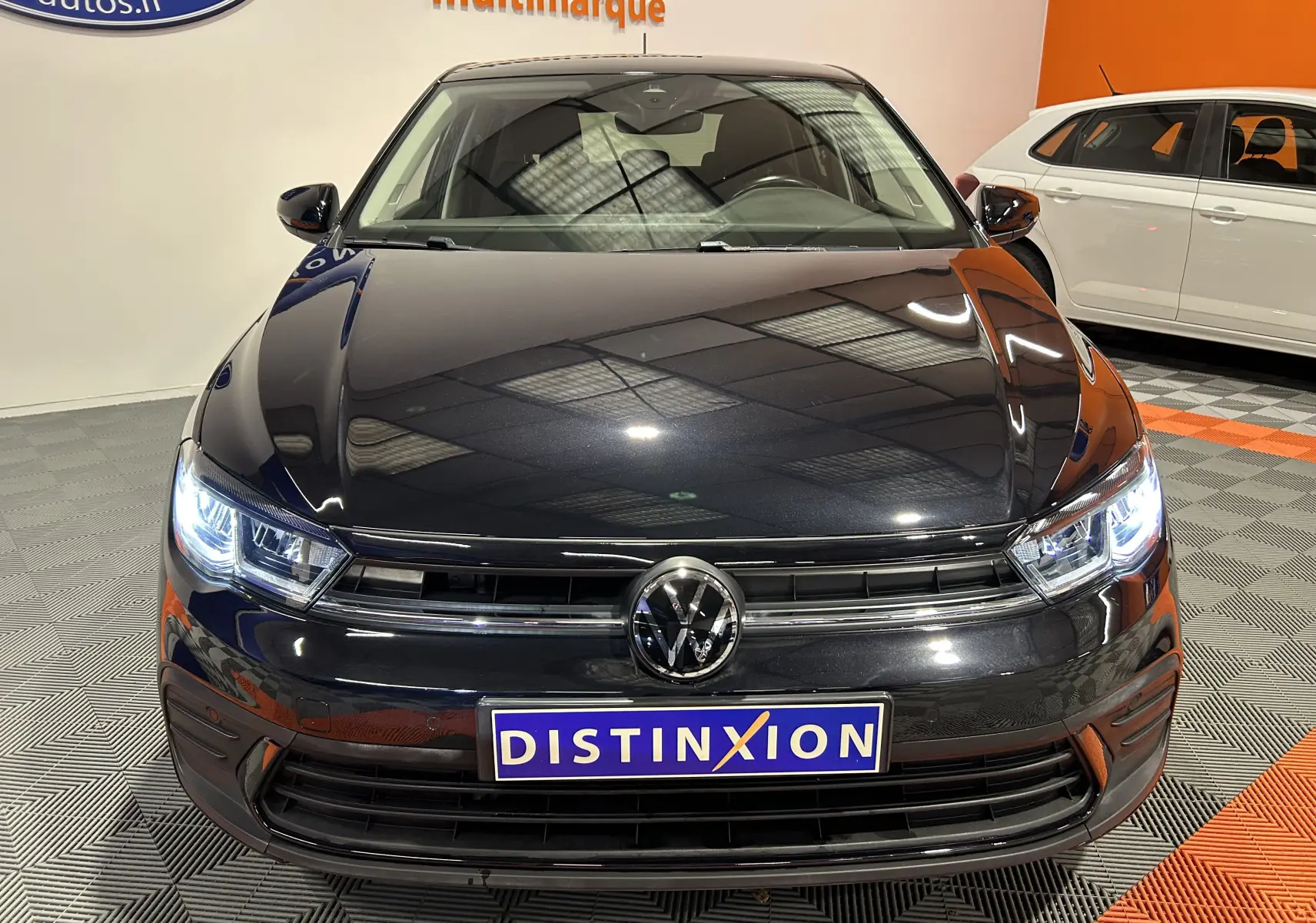 Vue avant d'une Volkswagen Polo noire 2022 avec phares allumés et calandre chromée dans un showroom.